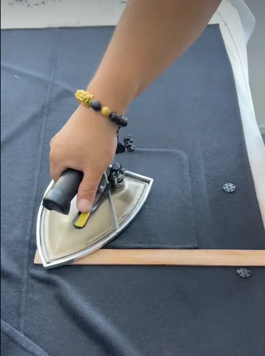 Worker steam pressing a dark fabric panel on the finishing table