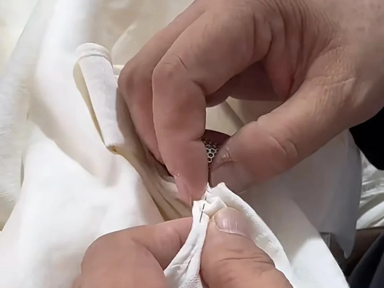 Hands completing a hand-finished detail on a white garment sample